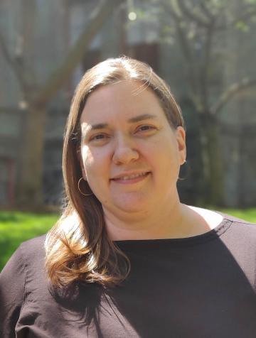 Photo of Angela Faranda. She is smiling and looking at the camera. Her brown hair is over one shoulder and she is wearing a black shirt. 