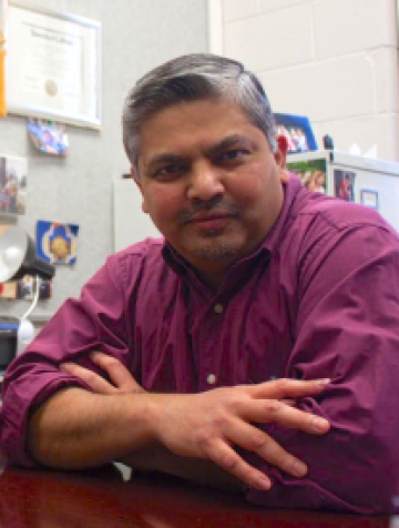 Rudra Sil sits with arms crossed looking into the camera. They have short salt-and-pepper hair and are wearing a magenta button-down shirt.