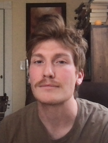 Nick Marziani, mustachioed, at his desk in his home office; behind him a bookshelf, a guitar, and a portrait of legendary crybaby Charles Bukowski. 