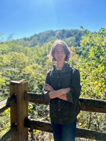 An image of Molly leaning against a fence, with forest in the background