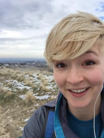 Outdoor headshot, woman with short blond hair standing and smiling in the mountains